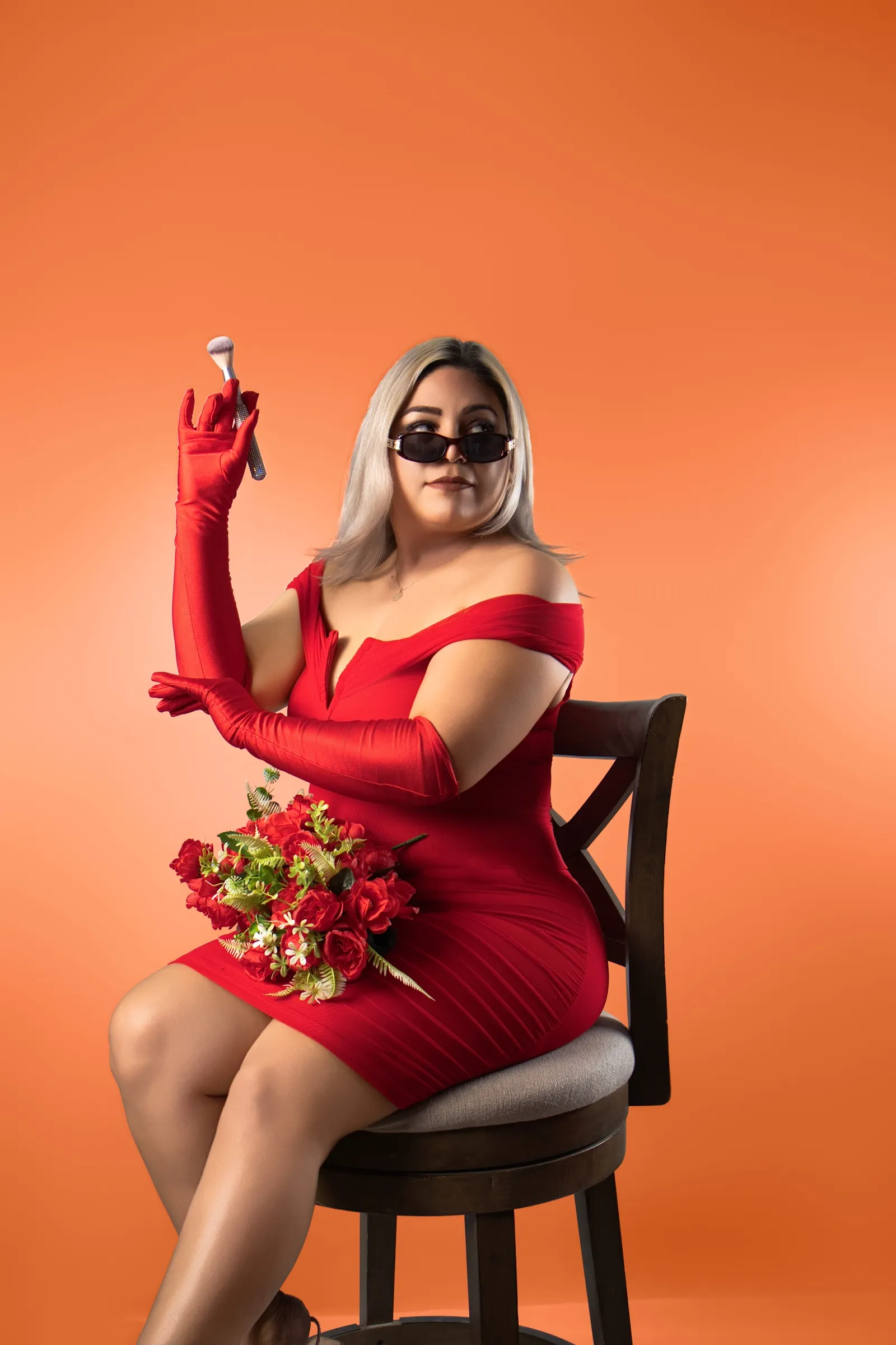 Adriana con lentes oscuros levanta una brocha, ramo de rosas en el regazo