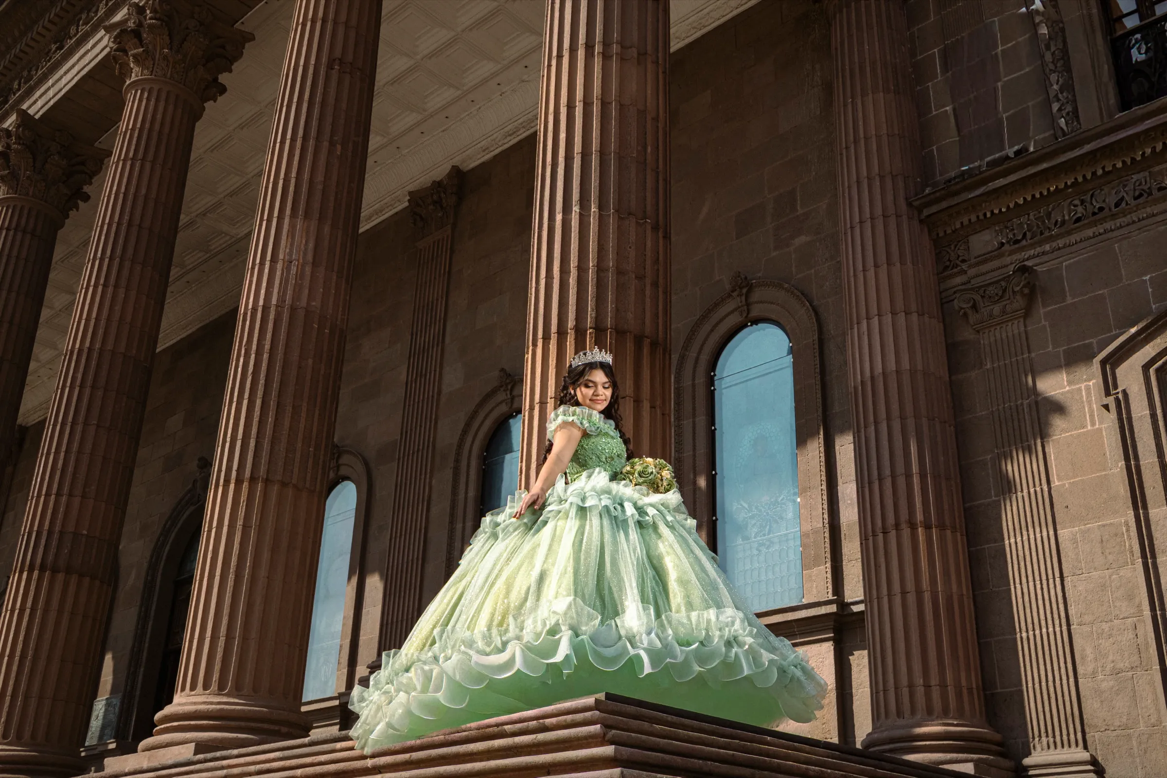 Quinceañera con vestido verde entre columnas de cantera