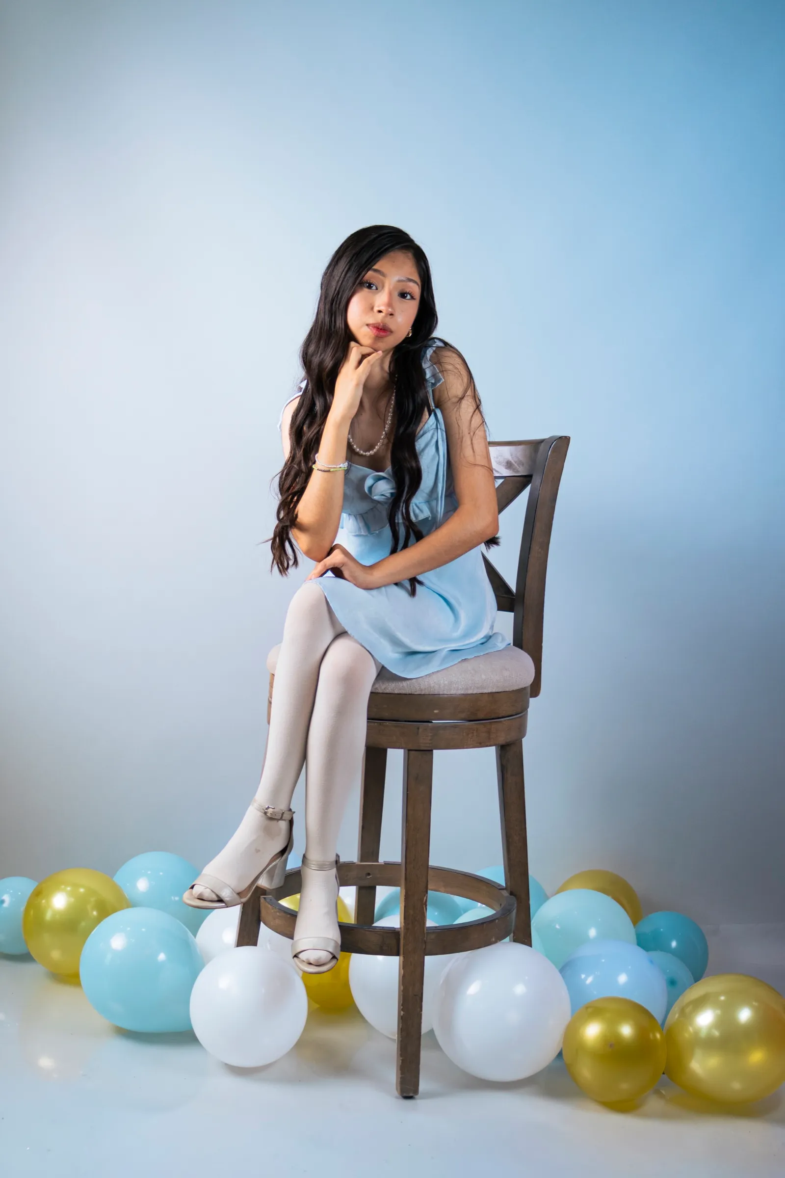 Libni sentada en un banco alto entre globos dorados y azules